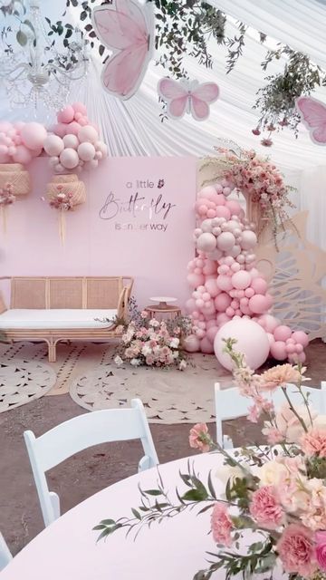 a pink and white party setup with balloons, flowers, and butterflies on the wall