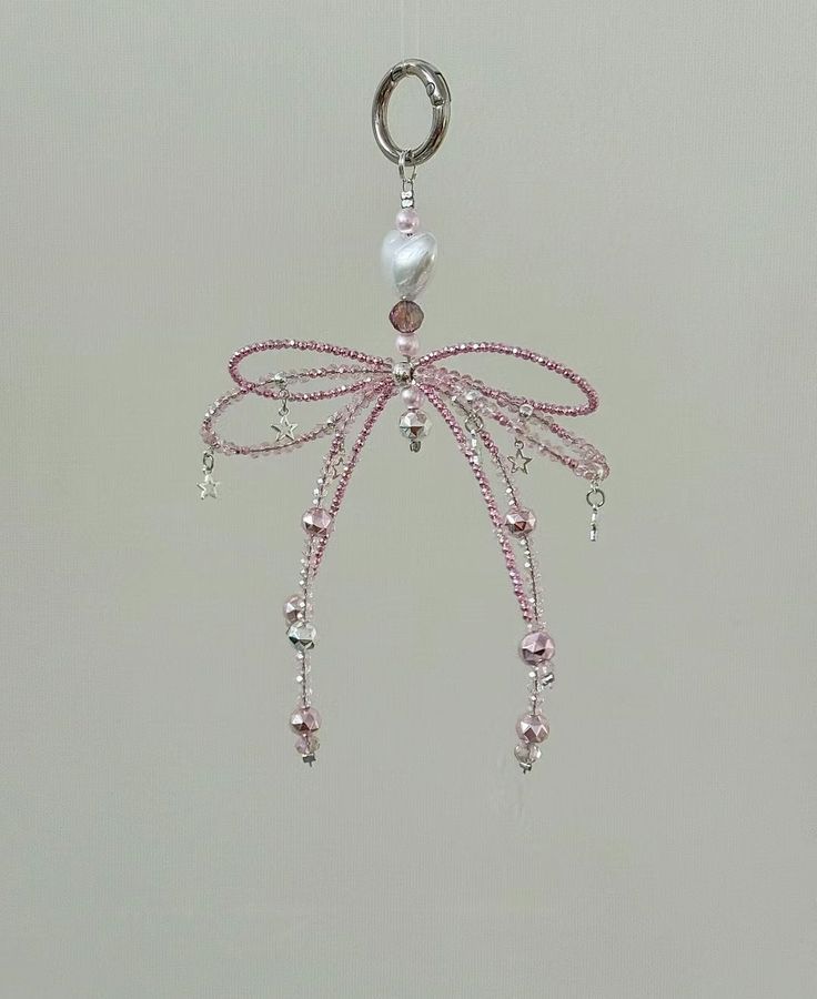 a pink beaded dragon keychain hanging from a hook on a white wall