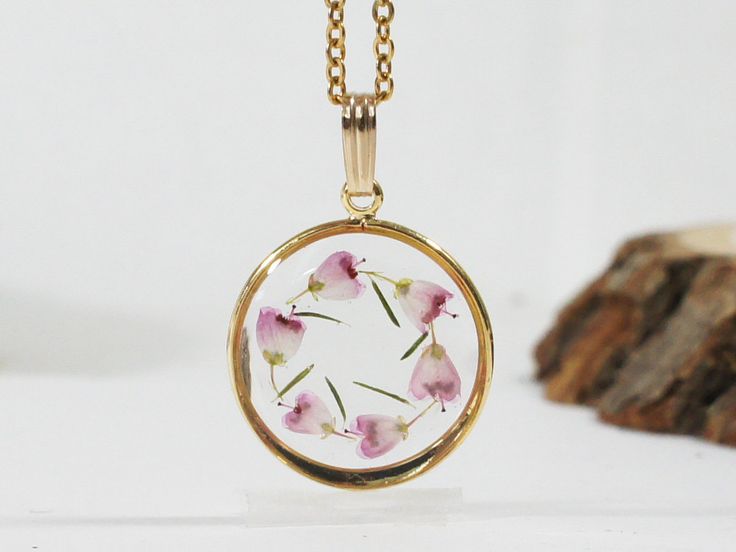 a necklace with pink flowers on it sitting next to a piece of wood