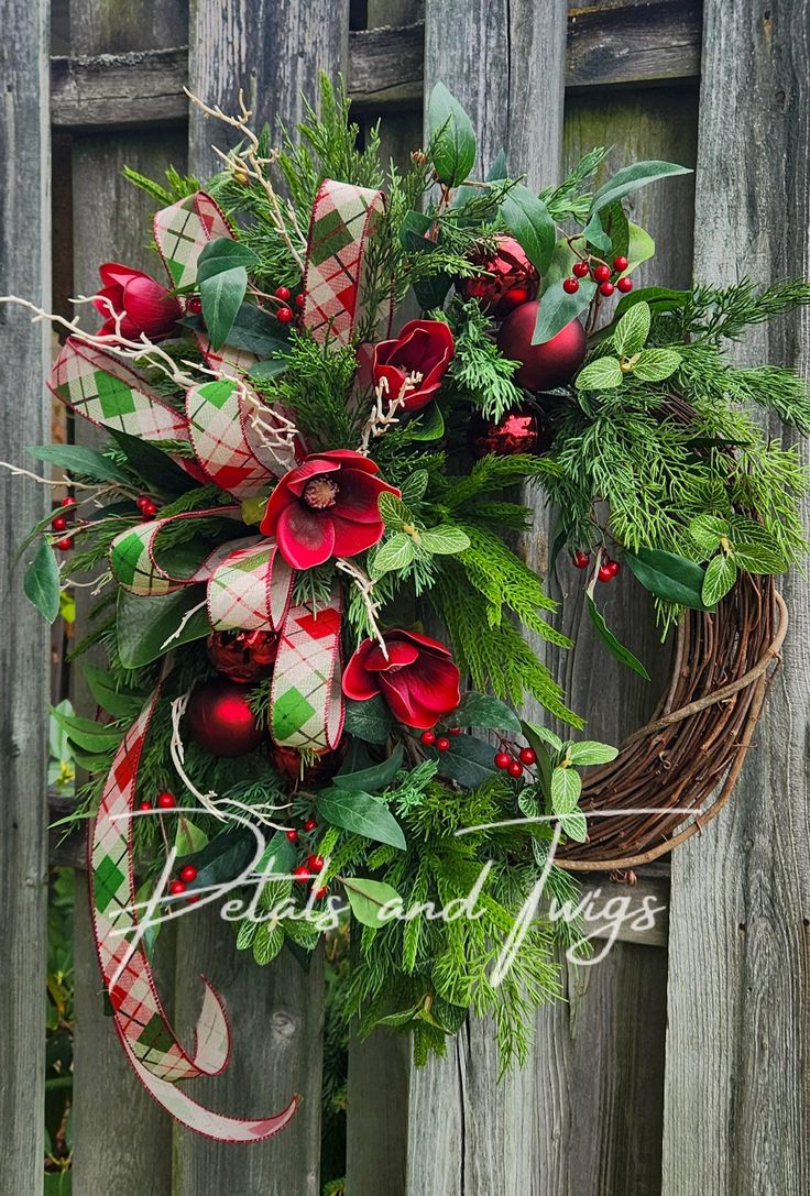 a wreath with red flowers and greenery hanging on a fence