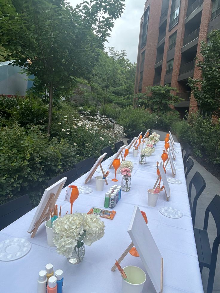 a long table is set up with white flowers and orange chairs for an outdoor event