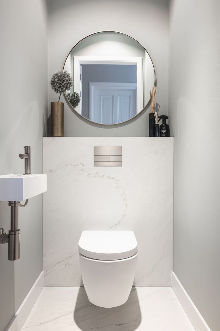 a white toilet sitting under a round mirror in a bathroom