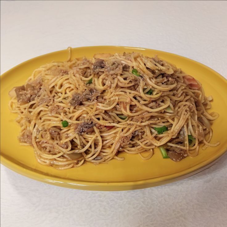 a yellow plate topped with noodles and meat