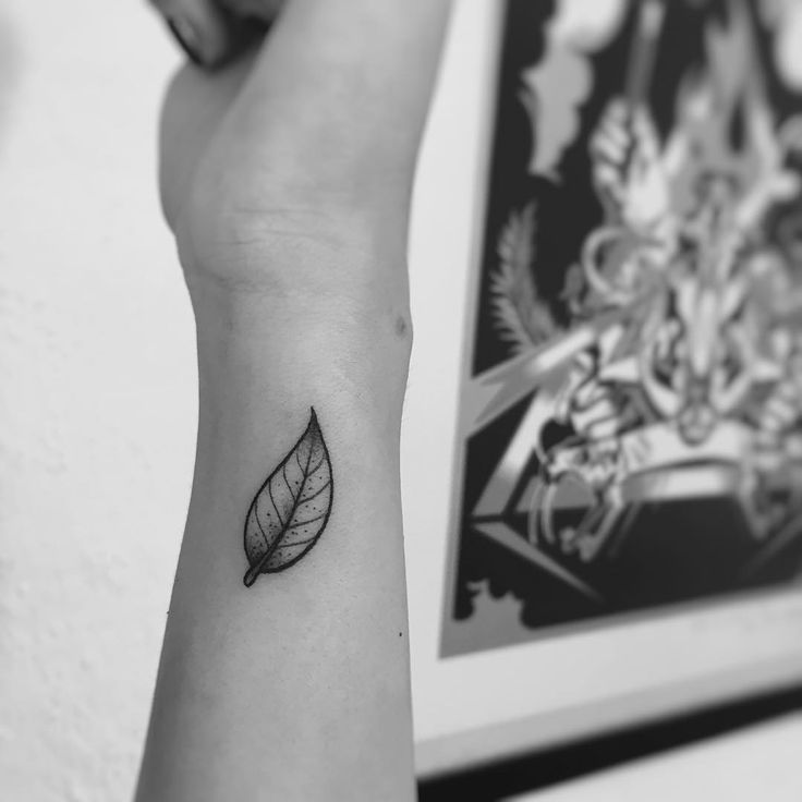 a black and white photo of a woman's arm with a leaf tattoo on it