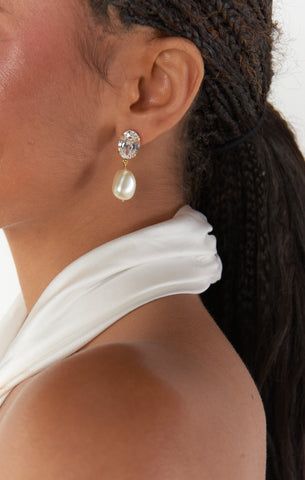 a close up of a person wearing ear rings and a white top with pearls on it