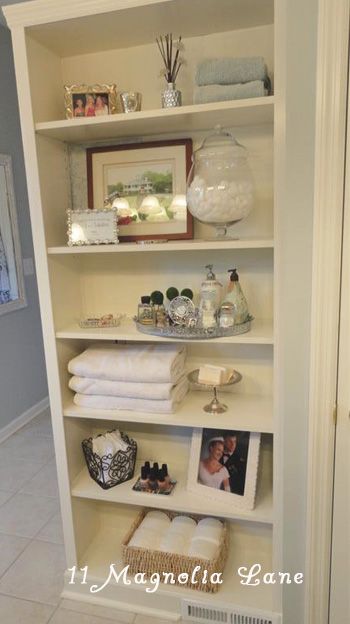 a white book shelf with pictures and other items on it's shelves in a bathroom