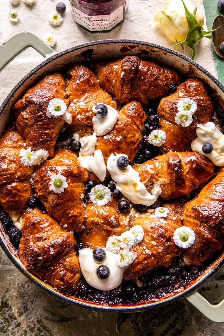 a pan filled with blueberries and cream covered croissants on top of a table