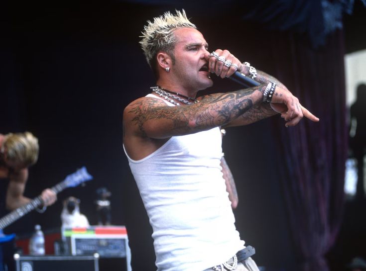 a man with tattoos on his arm holding a microphone in front of two other men