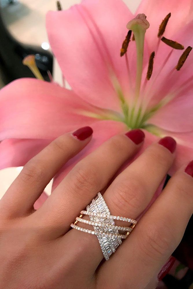 a woman's hand holding a pink flower with three diamond rings on her fingers