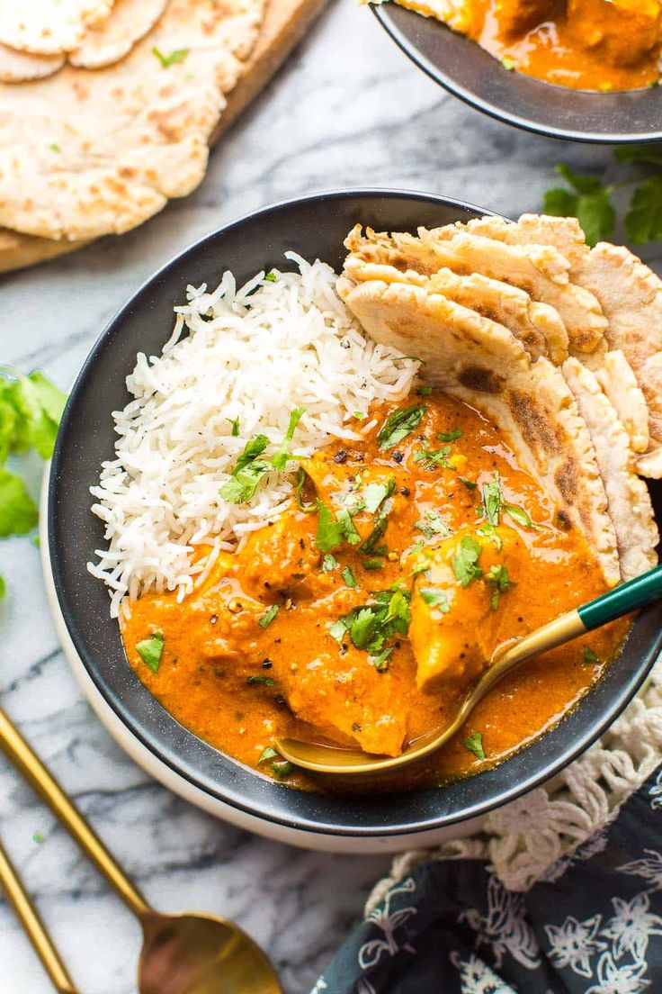 a bowl filled with rice and chicken curry next to pita bread on a table