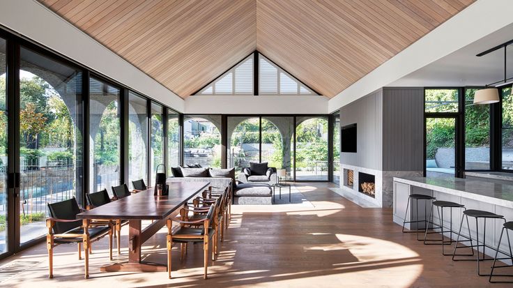 a large open living room and dining area with wood ceilinging, white walls, and windows