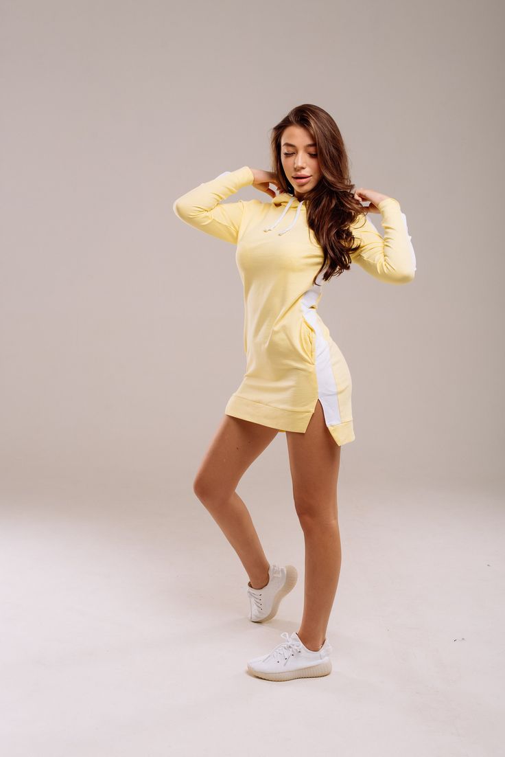 a woman posing in a yellow dress with her hands on her head and arms behind her back