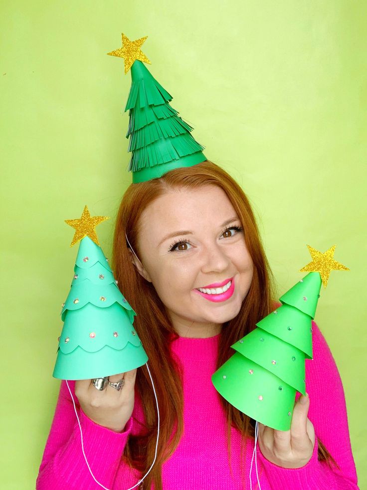 a woman in pink sweater holding up two green christmas trees with gold stars on them