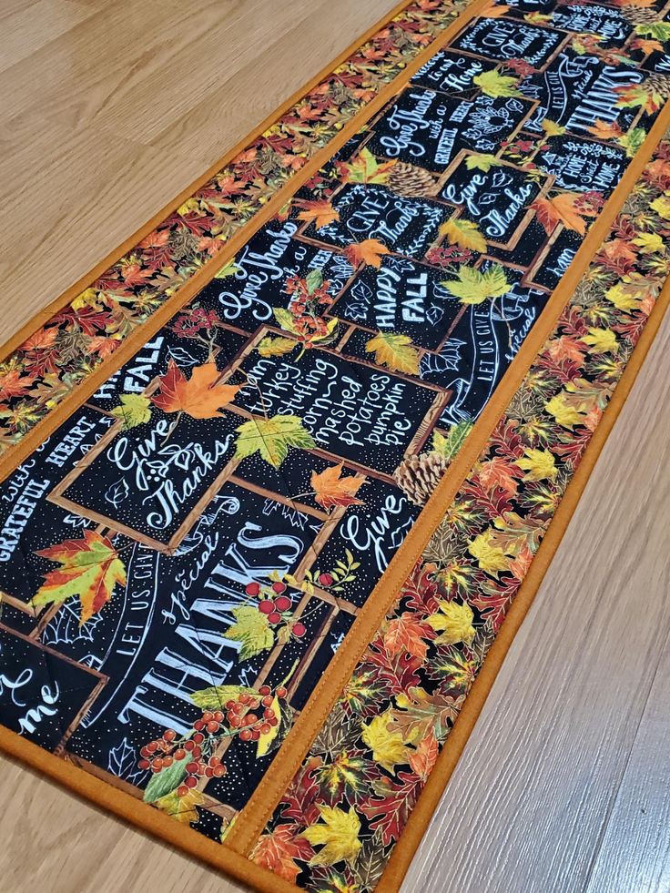 a table runner with fall leaves and chalkboard writing on the front, sitting on a wooden floor