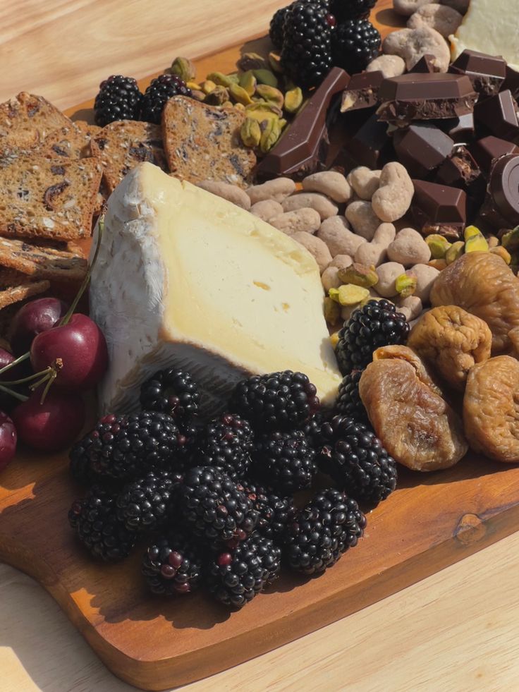 a wooden platter filled with cheese, crackers, and fruit on top of a table