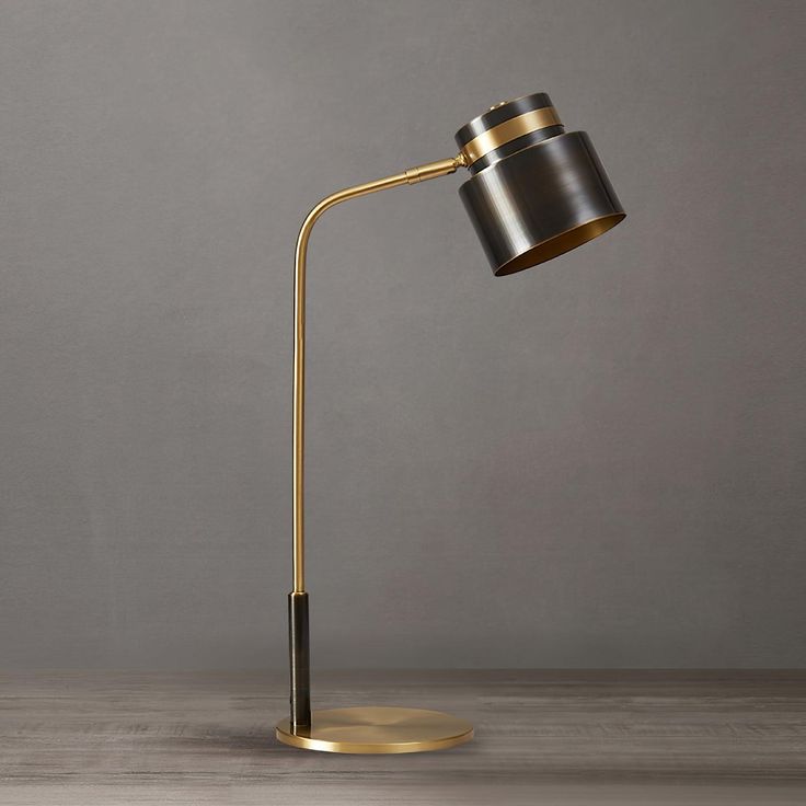 a black and gold floor lamp on a wooden table next to a gray wall in an empty room