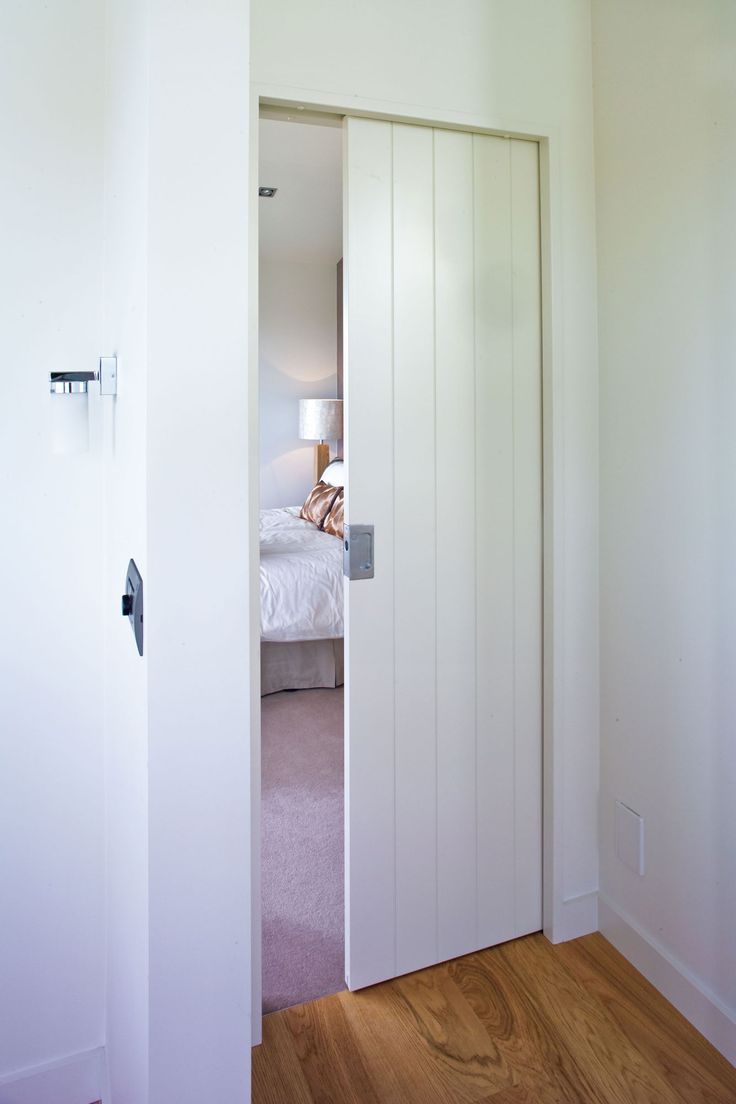 an open door leading to a bedroom with a bed in the background and hardwood flooring