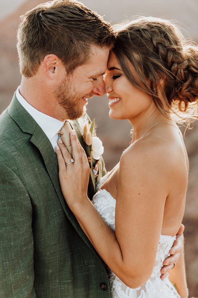 a bride and groom smile at each other while standing in front of the desert mountains