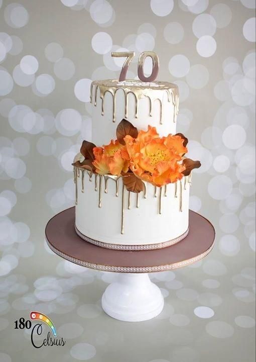 a white cake topped with orange flowers and dripping icing on top of a table