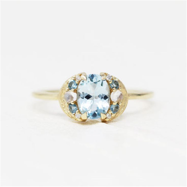 Discover the unique charm of the LeConte Impasto Collection with this handcrafted 14K yellow gold artisan fashion ring, size 6. Designed for those who appreciate the beauty of art and nature, this exquisite piece features a central 0.97ct oval aquamarine, enveloped by an array of stunning gemstones.Key Features:-Exceptional Craftsmanship: Each ring is a masterpiece from the LeConte Impasto Collection, reflecting the pinnacle of artisanal skill.-Captivating Centerpiece: A mesmerizing 0.97ct oval aquamarine takes center stage, symbolizing tranquility and eternal youth.-Elegant Accents: Complemented by 4=0.05tw round blue topazes and 2=0.01tw cabochon moonstones, adding layers of depth and intrigue.-Sparkling Diamonds: Embellished with 4=0.02tw round G/H SI1 diamonds, offering a subtle shimme Unique Yellow Gold Oval Moonstone Ring, Unique Oval Yellow Gold Moonstone Ring, Unique Oval Moonstone Ring In Yellow Gold, Unique Oval Yellow Gold Topaz Ring, Unique Oval Birthstone Ring, Unique Oval Cluster Ring In Yellow Gold, Luxury Blue Oval Moonstone Ring, Unique Oval Sapphire Ring With Center Stone, Handmade Oval Sapphire Ring In 14k Gold