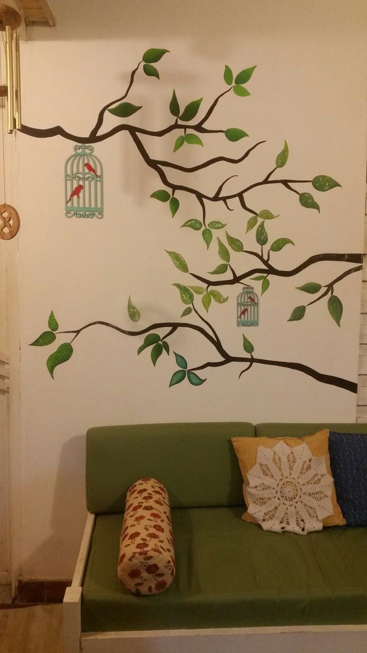 a green couch sitting in front of a tree with birdcages on it