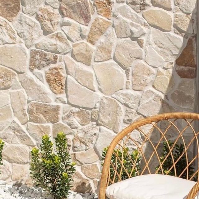 a wicker chair sitting in front of a stone wall with potted plants next to it