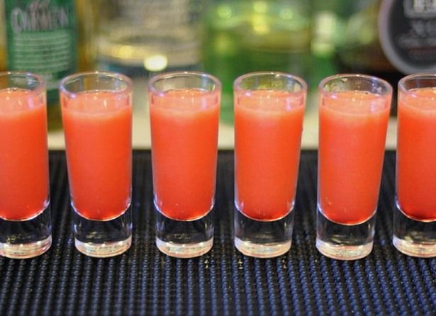 four shot glasses filled with orange juice on top of a table