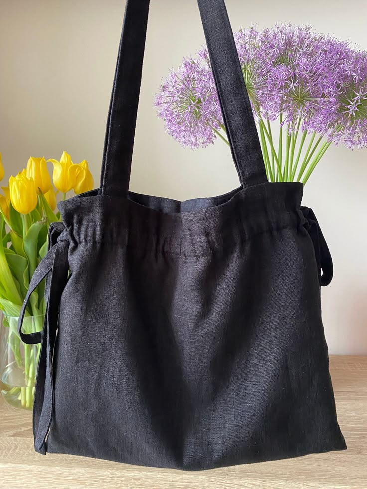 a black bag sitting on top of a wooden table next to yellow and purple flowers