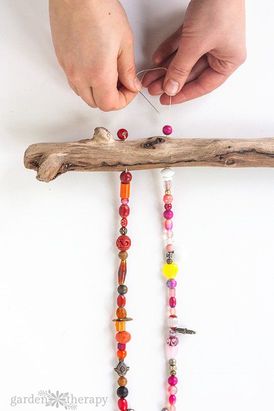 a person making beaded necklaces on a piece of driftwood next to a stick