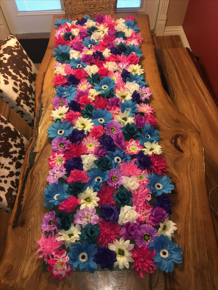 a long table covered in colorful flowers on top of a hard wood floor next to a window