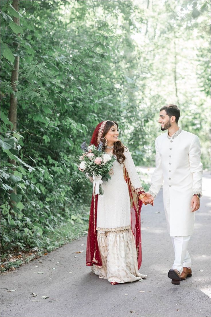 a bride and groom holding hands walking down the road in front of some green trees