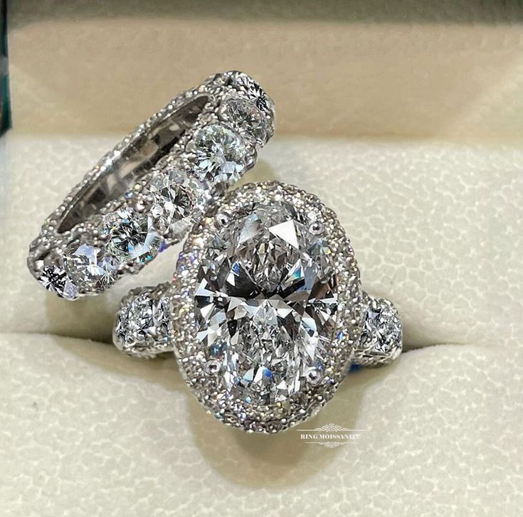 two diamond engagement rings sitting on top of a white cloth covered box with diamonds in it