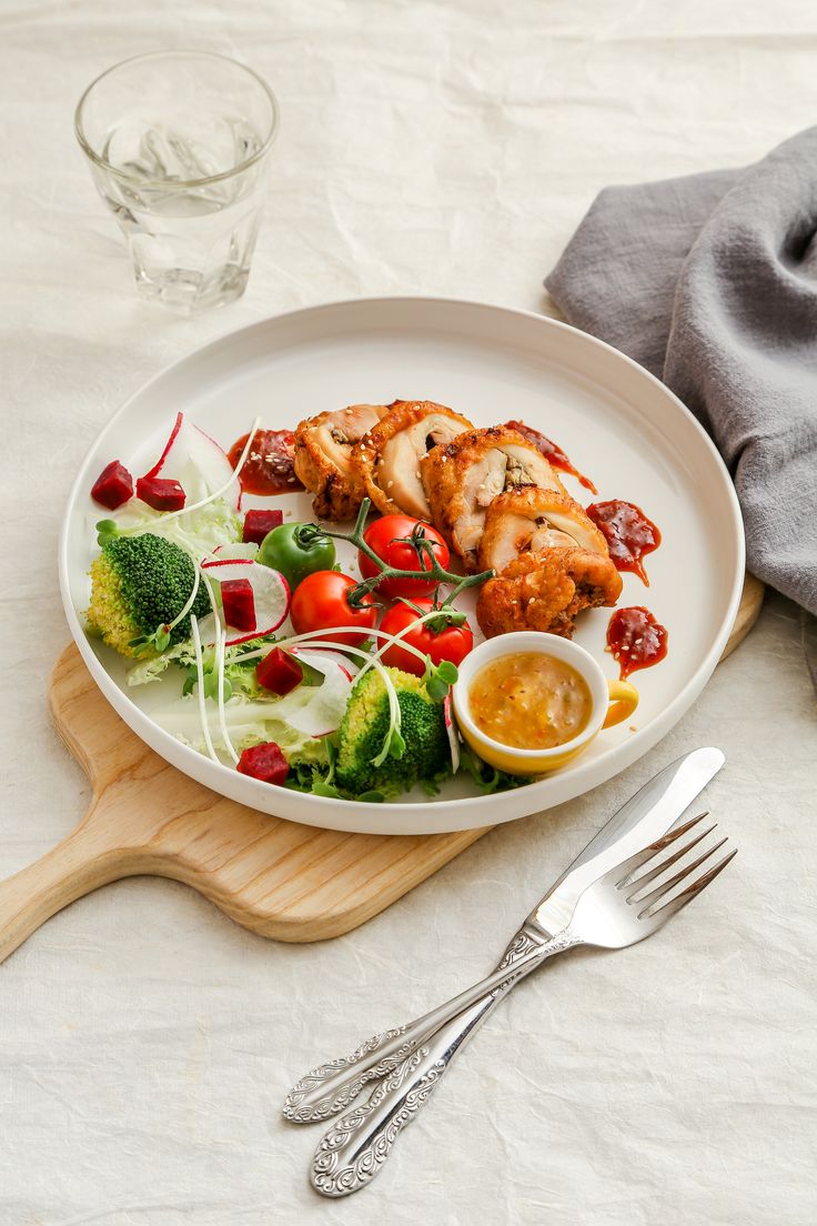 a white plate topped with meat and veggies next to a glass of water