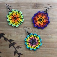 three beaded flower earrings sitting on top of a wooden table next to a plant