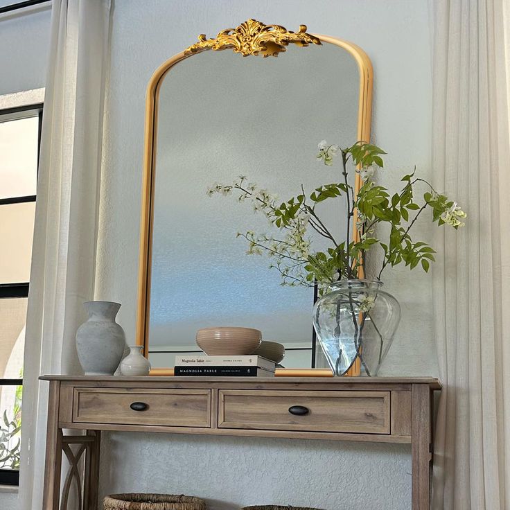 a wooden table topped with a mirror and vase filled with flowers