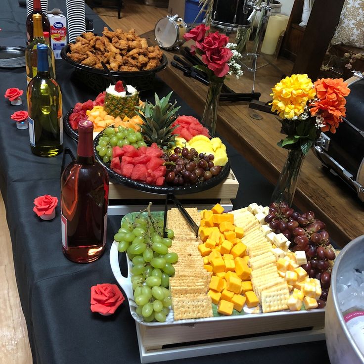 several trays of different types of food on a table with wine bottles and flowers