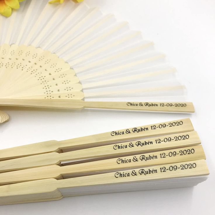 two wooden fans with engraved names on them and flowers in the background, sitting next to each other