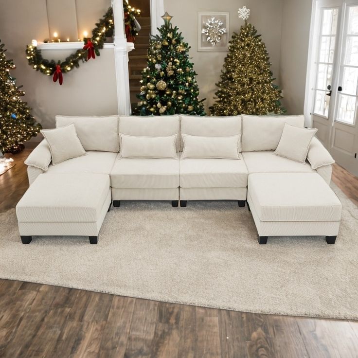 a white sectional couch sitting on top of a hard wood floor next to christmas trees