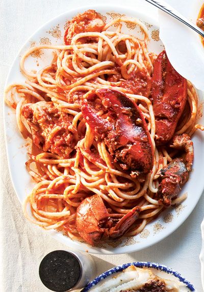 two plates of spaghetti with lobsters and sauce on the side next to some bread