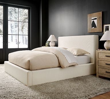 a white bed sitting on top of a wooden floor next to a dresser and window