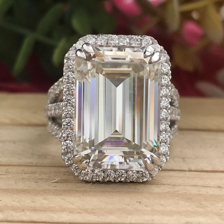 an emerald cut diamond surrounded by halos on a wooden surface with flowers in the background