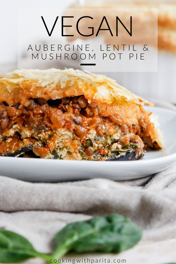 a white plate topped with meat and vegetable lasagna next to spinach leaves