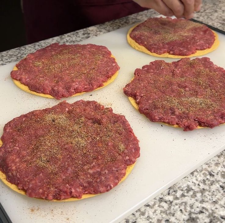 four hamburger patties on a baking sheet ready to go into the oven