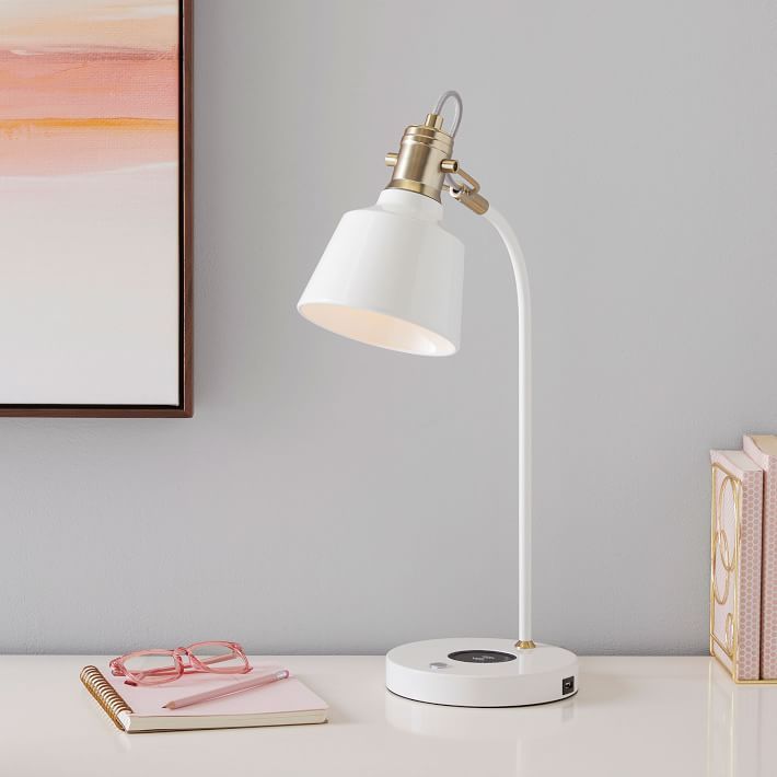 a white desk lamp sitting on top of a table next to a pink and yellow painting