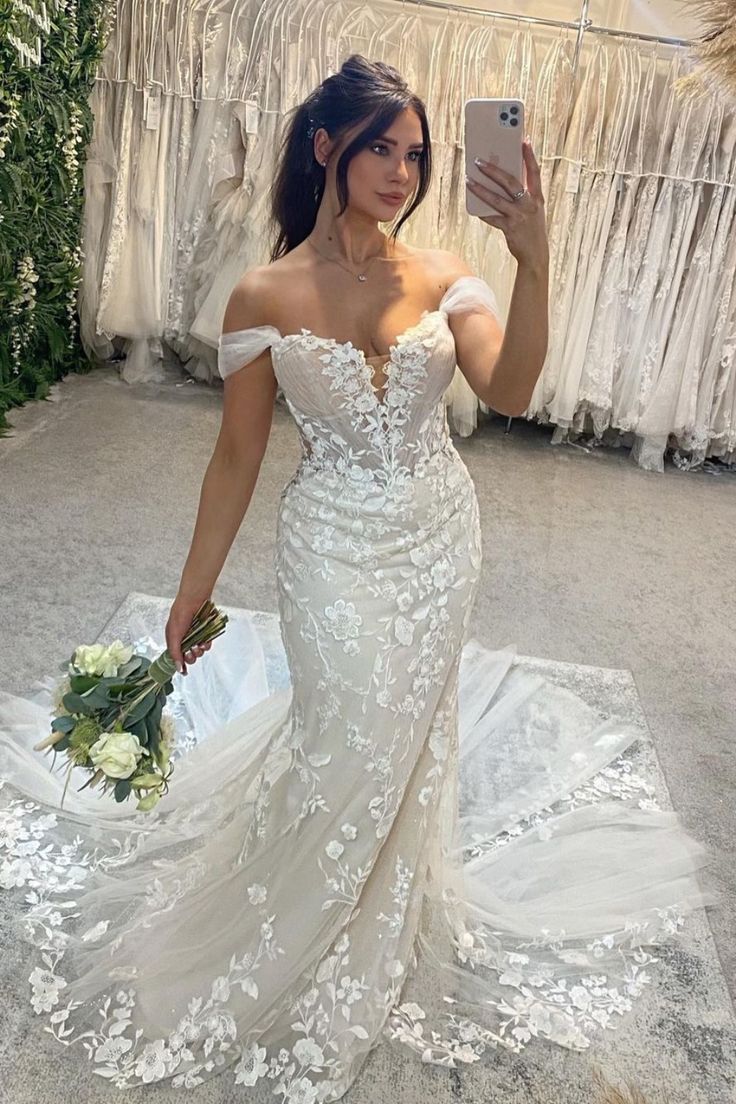 a woman in a wedding dress taking a selfie with her cell phone while holding a bouquet