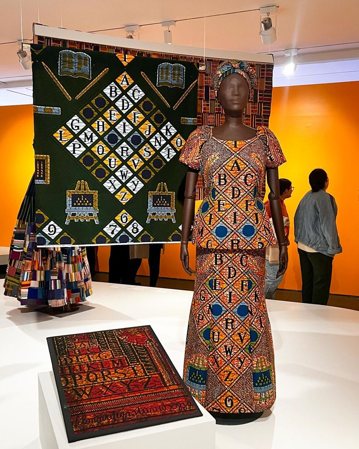 a woman is standing in front of an african art piece and two rugs on display