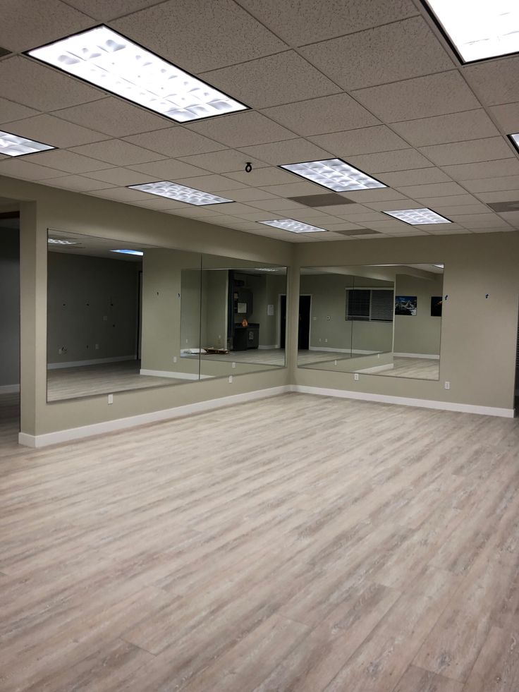 an empty room with several mirrors on the wall and wood flooring in front of it