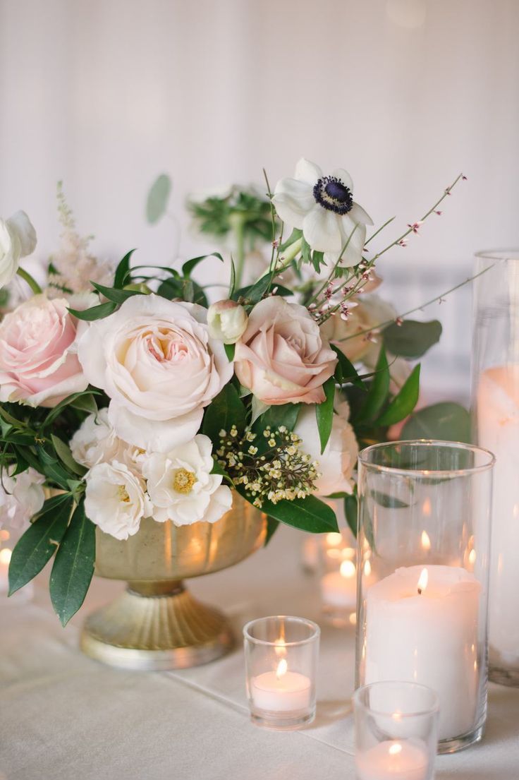 a table topped with candles and flowers on top of a white table cloth covered table