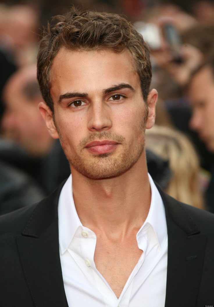 a man in a black suit and white shirt is looking at the camera with people behind him