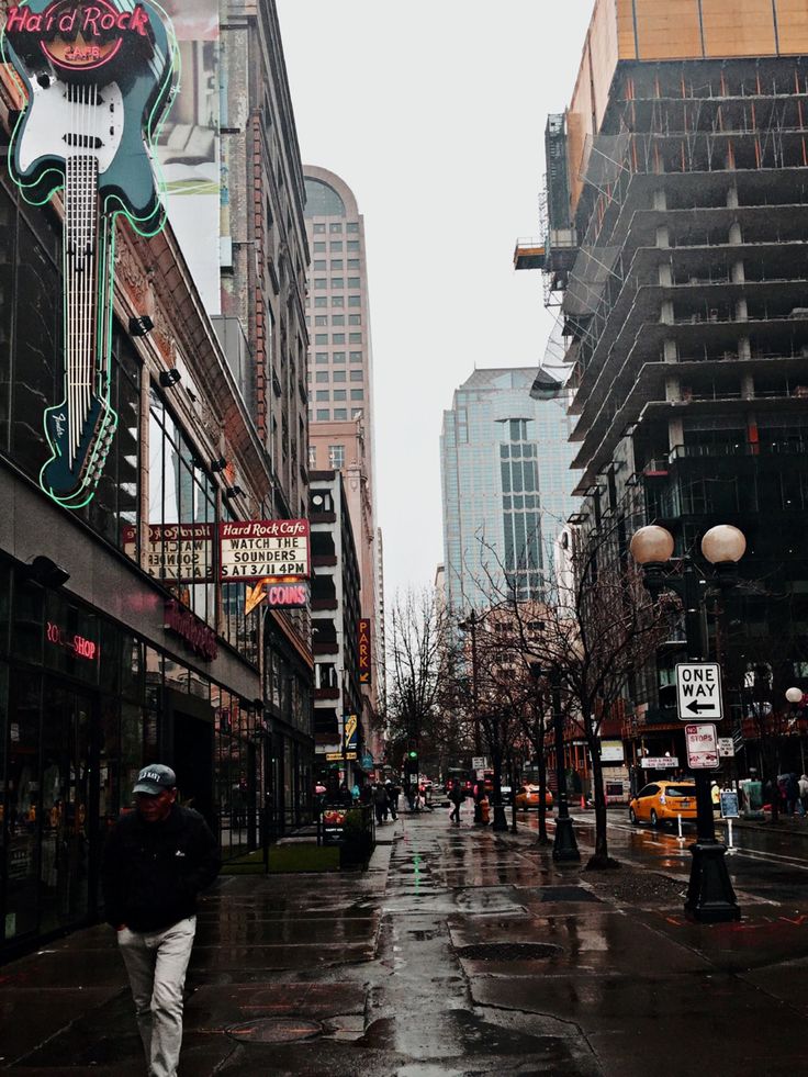 a man walking down a wet street next to tall buildings